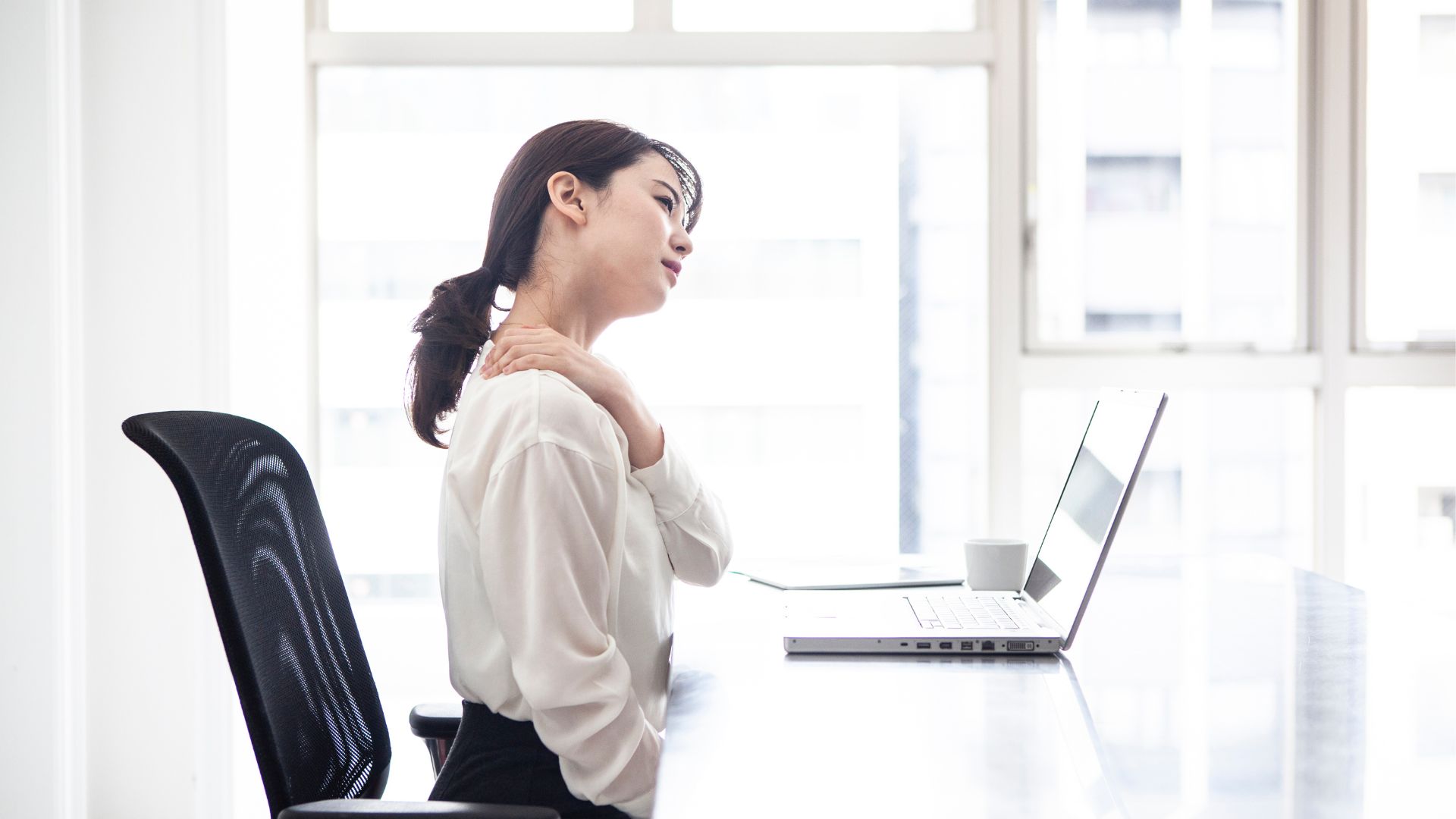 デスクワーク中に肩こりに悩む女性。chanvreが肩こり・腰痛ケアを提供。